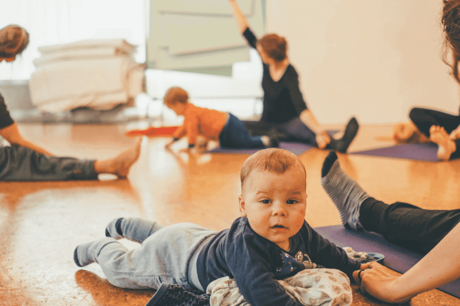 Kursgruppe mit Babys sitzt im Kreis und übt eine Yoga Seitdrehung im Sitzen