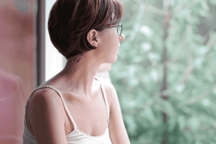 Frau mit Kurzhaarfrisur und Brille schaut verträumt aus dem Fenster