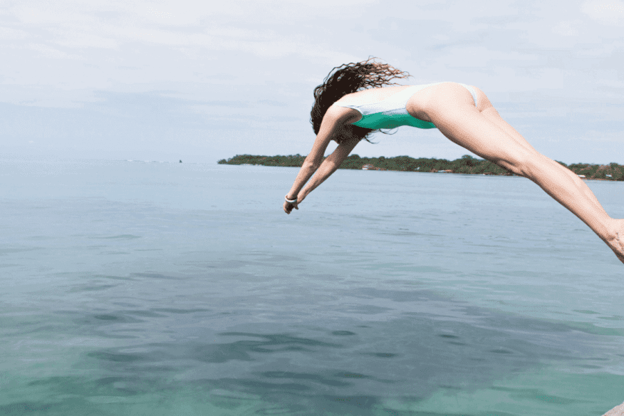 Eine Frau in blauem Badeanzug springt von einem Steg in einen See