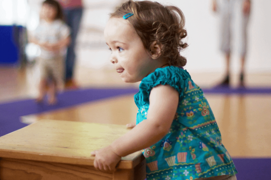 Ein anderthalbjähriges Kind schiebt im Tanzraum einen Tisch vor sich her