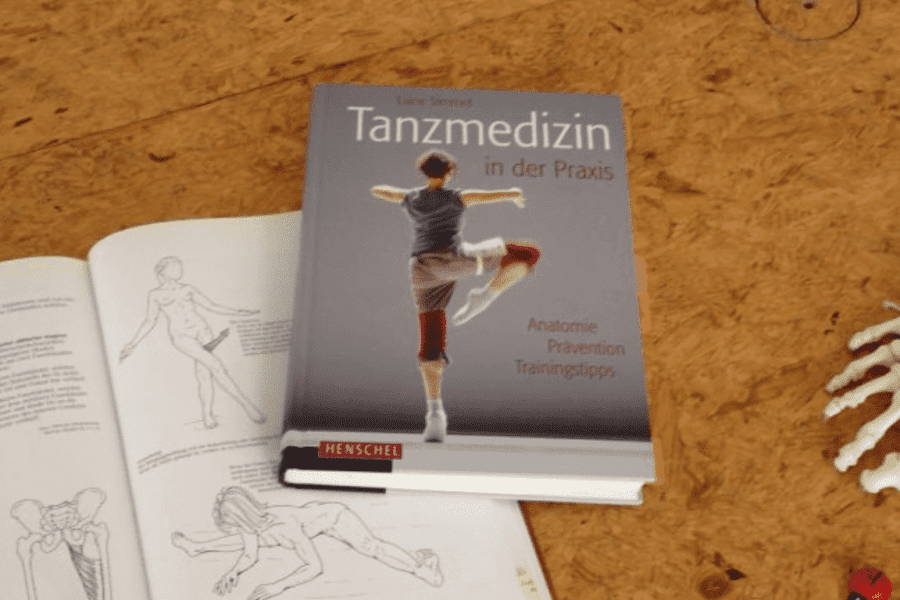 Ein Anatomiebuch über Tanztechnik und ein Fußskelettmodell liegen auf einem Tanzboden