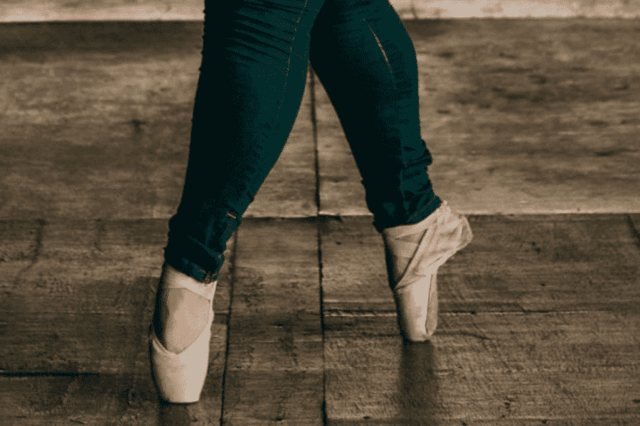 Ausschnitt zweier Beine in Spitzentanzschuhen, die Ballettbewegungen machen. Die Beine gehören offensichtlich zu einer übergewichtigen Frau.