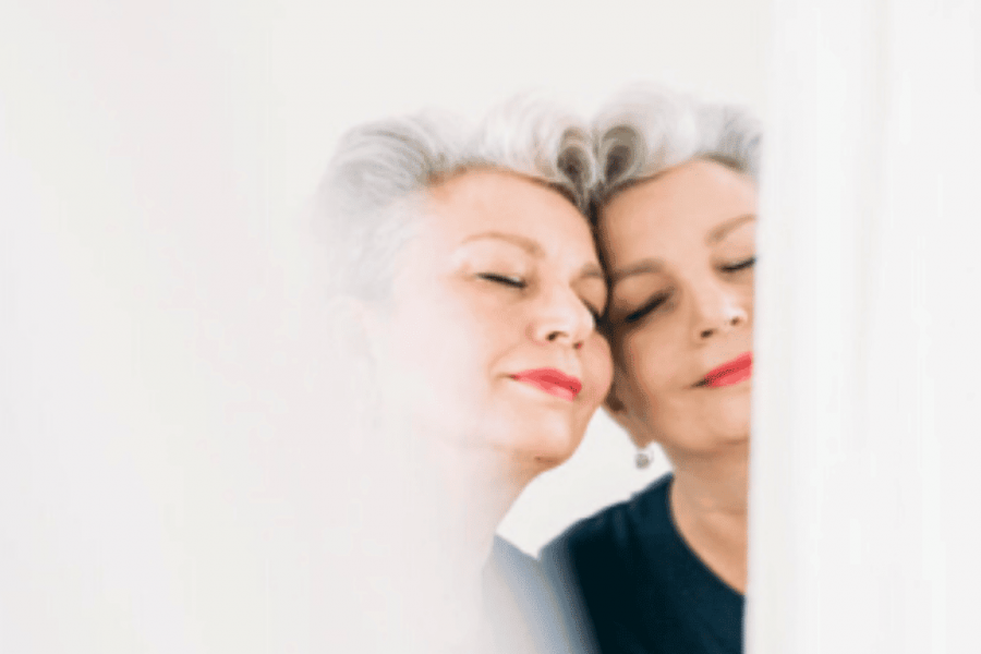 Eine ältere Dame mit weißem Haar lehnt verträumt und mit geschlossenen Augen an einem Spiegel