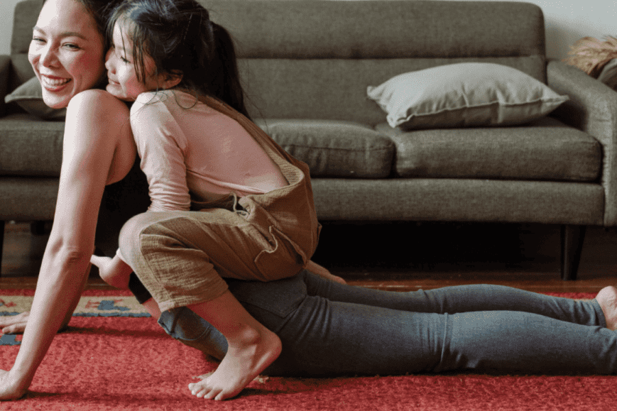 Eine Frau übt die Yoga-Kobra, während ihre Tochter auf ihrem Rücken liegt