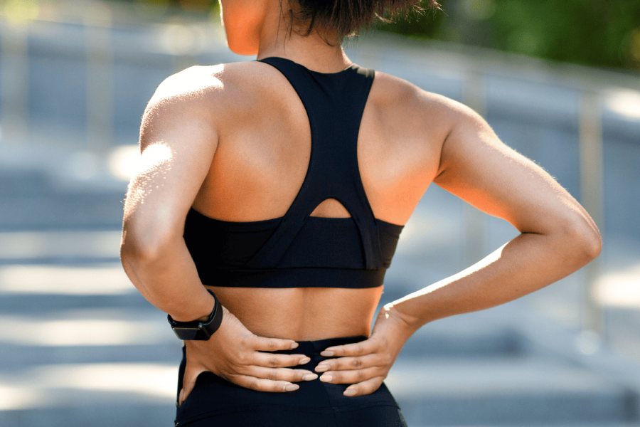 Die Ursachen für Rückenschmerzen sind meistens ungefährlicher Natur _ eine Sportlerin in schwarzem Sporttop hält sich den unteren Rücken