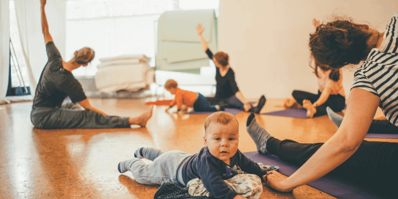 Mamas sitzen im Kreis und üben Yoga während die Babys um sie herumkrabbeln