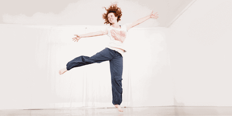 erwachsene Tänzerin macht im Tanzraum einen Sprung in die Luft, ein Bein ist zur Seite gestreckt, die Arme weit zur Seite gestreckt