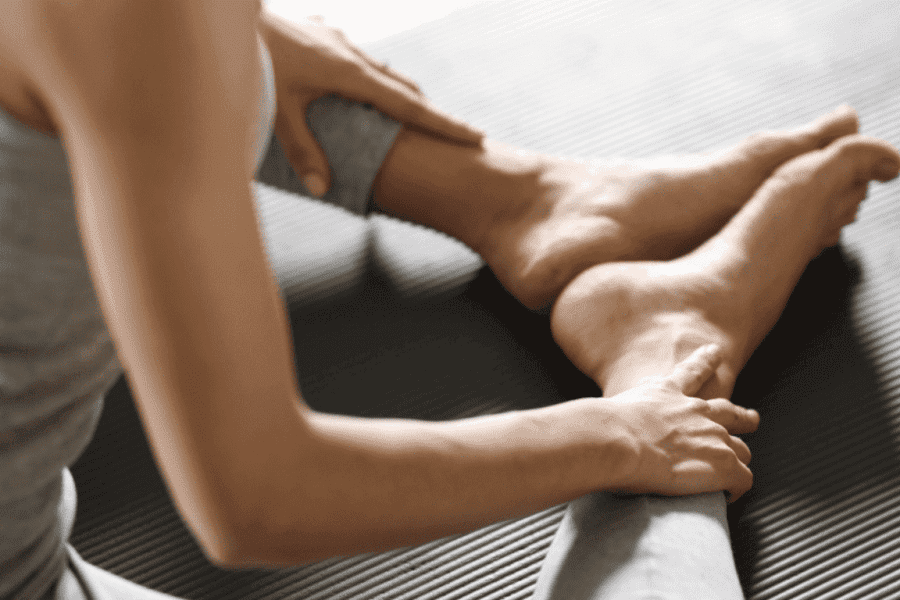 Eine Frau übt eine Beininnenseitendehnung auf einer grauen Pilatesmatte. Dazu sitzt sie mit gegrätschten Beinen, während sich ihre Fußinnenseiten berühren.