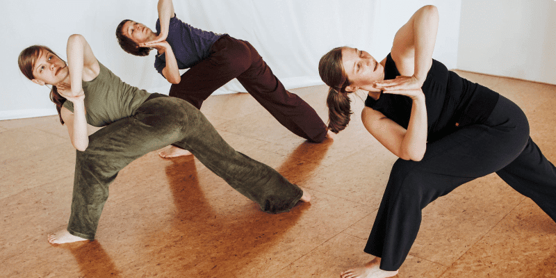 Drei Frauen in einer Stehhaltung aus dem Yoga, Hände Namaste, gedrehte Haltung